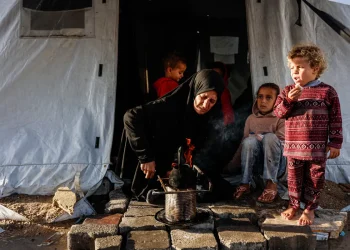 Una mujer calienta algo para comer en un campamento en Gaza/AFP