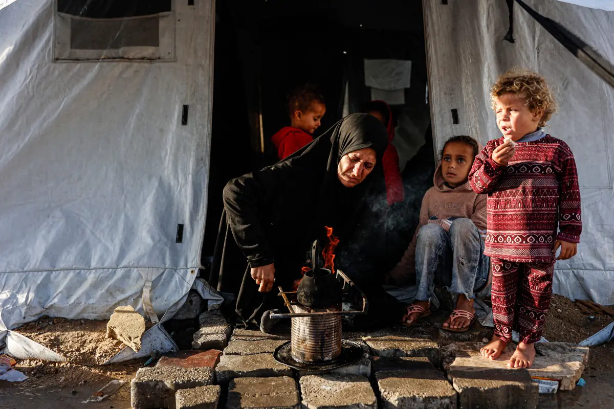 Una mujer calienta algo para comer en un campamento en Gaza/AFP