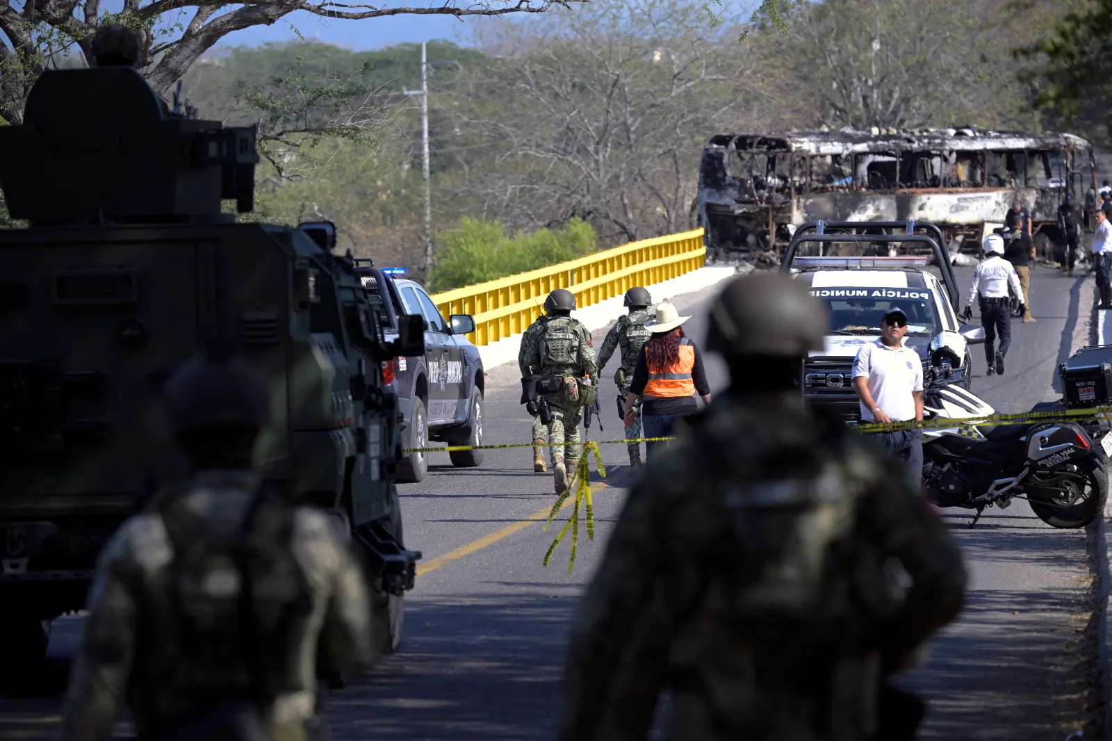 Operativo de seguridad en México tras la muerte del líder del CJNG, con fuerzas federales resguardando un puente y un autobús incendiado al fondo.
